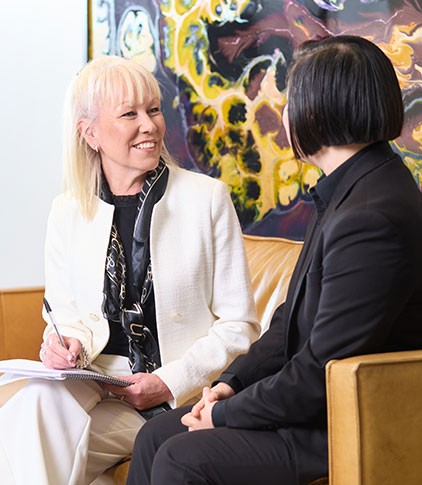 Paula Abbott having a focused business conversation with a client, both seated comfortably on a vibrant yellow sofa